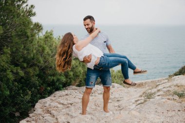 İspanyol bir adam, İspanya 'daki bir dağ parkında arka planda deniz varken Latin kız arkadaşını kollarında tutuyor. Valencia 'da deniz kenarında iki turist eğleniyor.