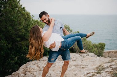 İspanyol bir adam, İspanya 'daki bir dağ parkında arka planda deniz varken Latin kız arkadaşını kollarında tutuyor. Valencia 'da gün batımında iki turist deniz kenarında eğleniyor.