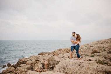 İspanyol bir adam ve Latin kız arkadaşı İspanya 'da bir dağ parkında kayalık deniz kıyısında sarılıyorlar. Valencia 'da iki turist eğleniyor..