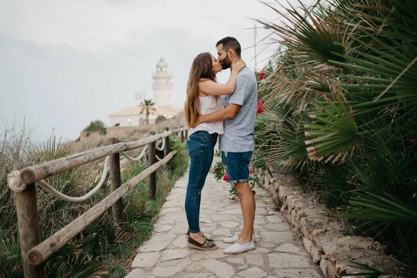 在西班牙 一位西班牙裔男子和他的拉丁女友在棕榈树之间的灯塔前亲吻对方 在瓦伦西亚 两名游客在日落时分互相欣赏 — 图库照片
