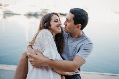 İspanyol bir adam gülümseyen esmer kız arkadaşını tutarken her ikisi de akşam İspanya 'da iskelede oturuyor. Valencia 'da gün batımında bir çift turist..