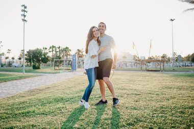 İspanya 'da akşamları İspanyol sevgilisiyle palmiye ağaçları ve güneş ışığı arasında gülen bir kızın tam boy fotoğrafı. Valencia 'da gün batımında bir çift turist..