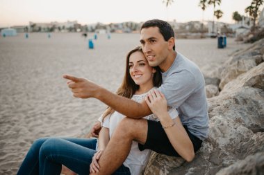 Bir kadın, İspanya 'da bir dalgakıranın taşlarının üzerinde İspanyol erkek arkadaşının bacaklarının arasında oturuyor. Bir adam gün batımında karısına sarılıyor. Adamın biri Valencia 'yı işaret ediyor..