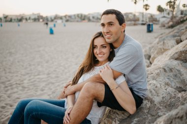 Bir kadın, İspanya 'da bir dalgakıranın taşlarının üzerinde İspanyol erkek arkadaşının bacaklarının arasında oturuyor. Bir adam gün batımında karısına sarılıyor. Valencia 'da randevusu olan iki turist..