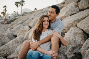 Bir kadın, İspanya 'da bir dalgakıranın taşlarının üzerinde İspanyol erkek arkadaşının bacaklarının arasında eğleniyor. Bir adam gün batımında karısına sarılıyor. Valencia 'da randevusu olan iki turist..