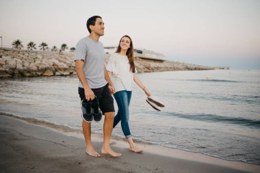 İspanya 'da, Balear Denizi' nin kıyısındaki kumlu bir plajda çıplak ayakla dolaşan, gülümseyen kız arkadaşıyla İspanyol bir adamın tam boy fotoğrafı. Valencia 'da randevusu olan iki turist.