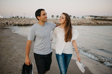 İspanyol bir adam ve gülümseyen kız arkadaşı akşam İspanya 'da Balear Denizi' nin kıyısında kumlu bir plajda dolaşırken sarılıyorlar. Valencia 'da randevusu olan iki turist..