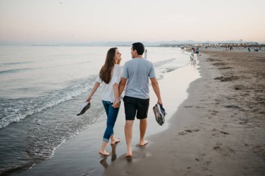 İspanya 'da alacakaranlıkta kumsalda çıplak ayakla eğlenen bir kadınla erkeğin fotoğrafı. Valencia 'daki Balearic Denizi' nin yakınlarında bir çift turist..