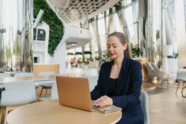Mavi ceketli bir kadın emlakçı bilgisayarın klavyesinde daktilo yazıyor. Modern lobide bir kadın masada oturuyor. Çağdaş bir ofis içinde dizüstü bilgisayarın yanında bir kadın bilişim geliştiricisi..