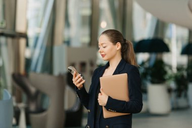 Dişi bir emlakçı dizüstü bilgisayar tutuyor ve cep telefonundan haber okuyor. Modern lobide güzel bir kadın duruyor. Bir iş kadını ofisinden çağdaş bir iç mekanda ayrılıyor..