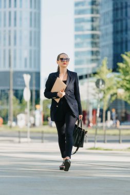 Blazer ceketli bir kadın emlakçı finans bölgesindeki ofis binaları arasında dizüstü bilgisayarla dolaşıyor. Bir iş kadını ofisinden yüksek binaların arasında ayrılıyor..