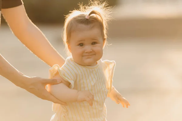 햇빛을 엄마의 안기는 아기의 사진이다 어머니는 딸에게 공원에서 첫걸음마를 가르치고 — 스톡 사진
