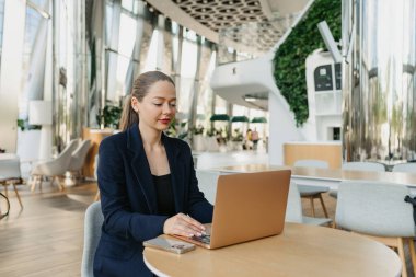 Mavi ceketli bir kadın emlakçı bilgisayarın klavyesinde daktilo yazıyor. Modern lobide bir kadın masada oturuyor. Çağdaş bir ofis içinde dizüstü bilgisayarın yanında bir kadın bilişim geliştiricisi..