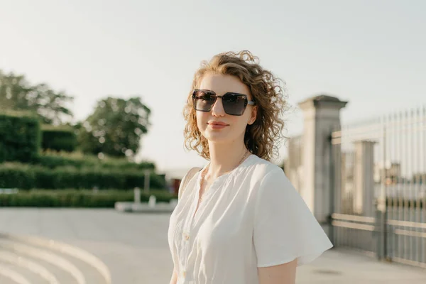 Žena Kudrnatými Vlasy Slunečních Brýlích Bílými Šaty Pózuje Parku Při — Stock fotografie