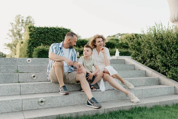 Father, mother, and son are sitting on the steps in the garden of an old European town. Happy family in the evening. Dad is discussing important themes with his family in the park at sunset.