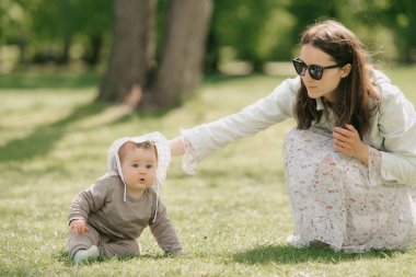 Genç bir anne, yedi aylık kızıyla çayırda oynuyor. Küçük bir kız çimlerin üzerinde sürünüyor..