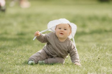 Beyaz panama şapkalı 7 aylık bir çocuk çayırda eğleniyor. Küçük bir kız çimlerin üzerinde sürünüyor..