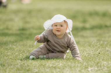 Beyaz panama şapkalı 7 aylık bir çocuk çayırda eğleniyor. Küçük bir kız çimlerin üzerinde sürünüyor..