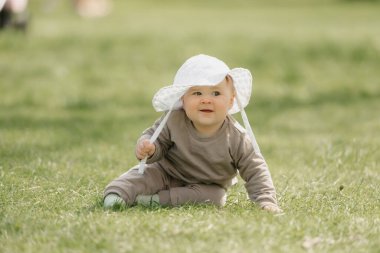 Panama şapkalı 7 aylık gülümseyen bir çocuk çayırda güneşleniyor. Küçük bir kız çimlerin üzerinde sürünüyor..