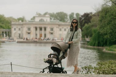Bir anne bebeğiyle birlikte sarayın bölgesinde bebek arabasında poz veriyor. Parkta arka planda klasik mimari olan, bebek taşıyan bir anne..
