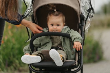 Bulutlu bir günde bebek arabasında bir bayan çocuk oturuyor. Yeşil bir köyde, yağmurluk giyen ciddi bir kız bebek arabasında. Bir anne kızının ceketine dokunuyor..