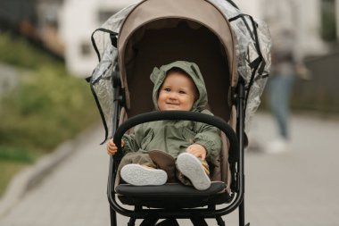 Mutlu bir bayan bebek puslu bir günde bebek arabasının tampon çubuğunu tutuyor. Yağmurluklu genç bir kız öğle vakti bir parkta bebek arabasında..