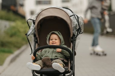 Bulutlu bir günde, bebek arabasında bir bayan bebek seviniyor. Yağmurluklu genç bir kız öğle vakti bir parkta bebek arabasında. Arka planda oğlu olan bir kaykaycı baba..