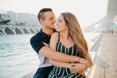 Gülümseyen bir çift turist Valencia 'da gün batımında su havuzu kenarında eğleniyor. Bir adam akşam kız arkadaşına sarılıyor. Kız İspanya 'da erkek arkadaşının bacağının üzerinde oturuyor.