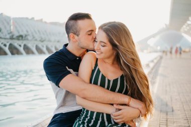 Gülümseyen bir çift turist Valencia 'da gün batımında su havuzu kenarında eğleniyor. Bir adam akşam kız arkadaşını öpüyor. Kız İspanya 'da erkek arkadaşının bacağının üzerinde oturuyor.