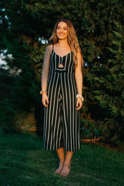 Valencia 'da günbatımında arka planda yeşil çalılarla poz veren gülümseyen bir kızın tam boy fotoğrafı..