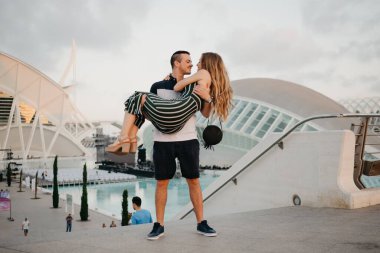 Birkaç turist, arka plandaki modern kentsel alanla Valencia 'da gün batımında eğleniyor. İspanya 'da akşam vakti bir adam kız arkadaşını elinde tutuyor.