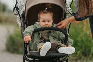 Bulutlu bir günde bebek arabasında bir bayan çocuk oturuyor. Yeşil bir köyde, yağmurluk giyen ciddi bir kız bebek arabasında. Bir anne kızının ceketine dokunuyor..