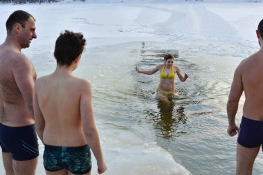 Kyiv, Ukraine - January 19, 2021 - Celebration of Epiphany in Kyiv. Orthodox believers look at the woman coming out of the icy water of the Dnipro River. The air temperature is 13 degrees below zerow.