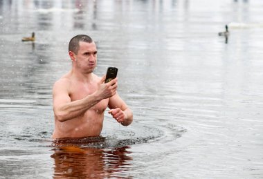 Kyiv, Ukraine - January 19, 2018 - A man makes a selfie on a phone while immersed in water of Dnipro River in Kyiv during the celebration of Epiphany