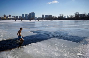 Kyiv, Ukraine - January 19, 2019 - A little boy comes into the ice hole in the shape of a cross in Kyiv during the celebration of Epiphany                                    