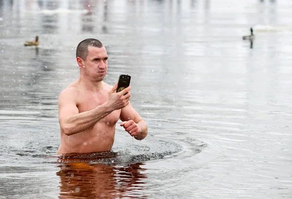 Kyiv, Ukraine - January 19, 2018 - A man makes a selfie on a phone while immersed in water of Dnipro River in Kyiv during the celebration of Epiphany