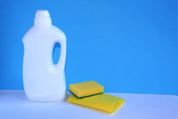 Uma garrafa com espaço vazio para fazer troça da embalagem do detergente sobre fundo branco azul com um pano e uma esponja para a limpeza das instalações. Ferramentas de limpeza, limpeza e limpeza. — Fotografia de Stock