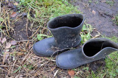 Siyah lastik botlar çamur ve su birikintisinde duruyor.