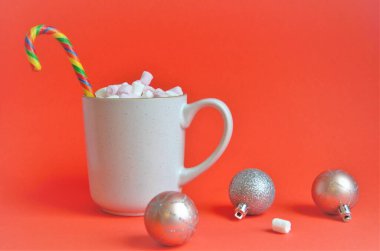 Marshmallow bardağı ve lolipop bastonu kırmızı arka planda Noel toplarıyla