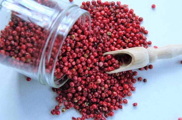 Pembe biber, beyaz arka planda cam bir kavanozdan serpilmiş kırmızı bezelyeler.