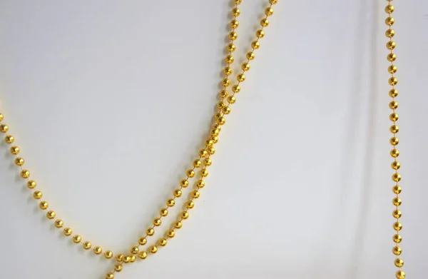 Su uno sfondo bianco, una catena di perline d'oro pende arbitrariamente, lo sfondo — Foto Stock