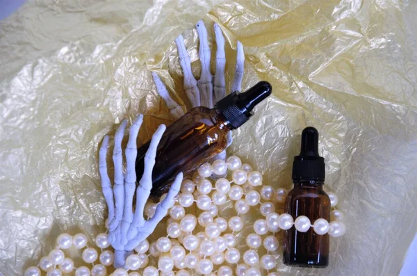 Mains d'un squelette avec des perles tenant une bouteille cosmétique sur un fond doré — Photo