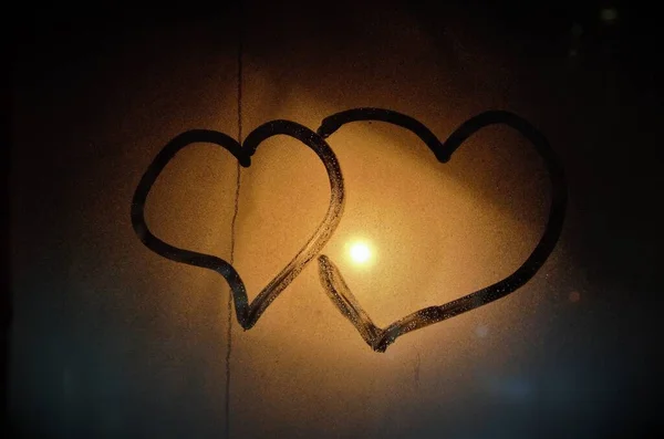 Two hearts on the glass fogged up with the light from the street lamp — Stock Photo, Image