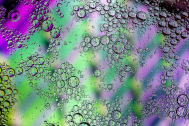 Suda yüzen yeşil ve pembe yağ damlalarının makrosu soyut, parlak daireler ve kabarcıklar oluşturuyor.