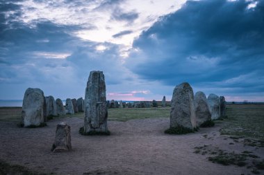 Ales stones in Osterlen in Sweden, a mystical rock formation from the early iron age. A night view with twilight from the pink colored setting sun and a dark overcast sky clipart