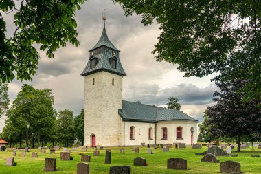 İsveç kırsalında taştan yapılmış eski beyaz kilise. Bir sürü mezar taşı olan yemyeşil bir mezarlık.,
