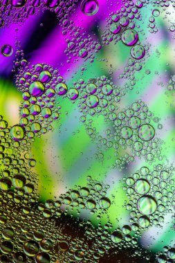 Suda yüzen yeşil ve pembe yağ damlalarının makrosu soyut, parlak daireler ve kabarcıklar oluşturuyor.