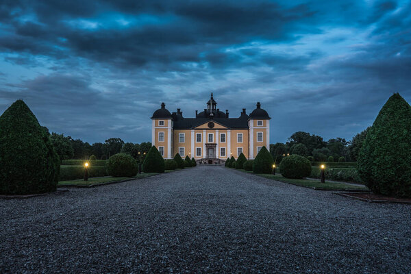 Spooky view of the beautiful yellow castle of Stromsholm in Sweden with its beautiful court yard and garden,  in summer night light and a cloudy overcast sky