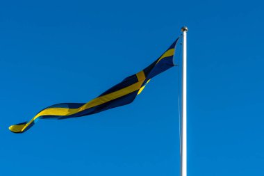 İsveç bayrağı açık mavi gökyüzüne karşı rüzgarda sallanıyor.