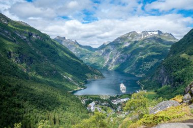 Norveç 'teki Geiranger fiyordunun üzerinde güzel bir yaz manzarası güneşli bir yaz gününde dik dağ kenarları. Körfeze demir atan büyük bir okyanus gemisi.